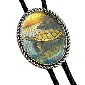 May include: A silver bolo tie with a round, glass pendant featuring a stained glass style image of a sea turtle swimming in the ocean at sunset.