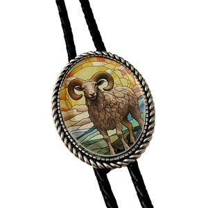 May include: A silver bolo tie with a round, stained glass pendant featuring a brown ram with curled horns against a colorful background.