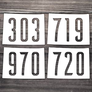 May include: Four white stencils with black numbers on a wooden background. The numbers are 303, 719, 970, and 720.