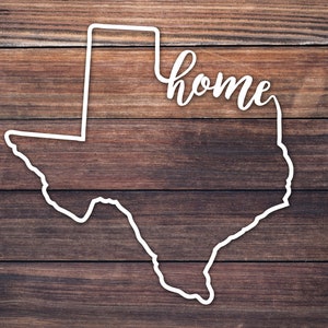 May include: White outline of the state of Texas on a brown wood background with the word "home" written in cursive above the state.