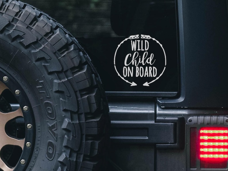 May include: A black car with a white vinyl sticker on the rear window that says "Wild Child On Board" in a circle with arrows pointing out.