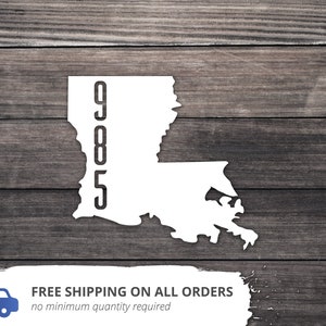 May include: White silhouette of the state of Louisiana with the numbers 905 printed vertically on the left side. The image is on a woodgrain background.