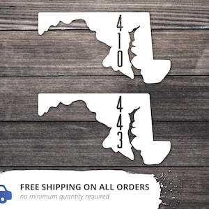 May include: Two white vinyl decals of the state of Maryland with the numbers 410 and 443 printed on them. The decals are on a wood background.