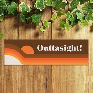 May include: A retro-style sticker with a sunset graphic and the text "Outtasight!" in white letters. The sticker has a brown background with orange, yellow, and white stripes.