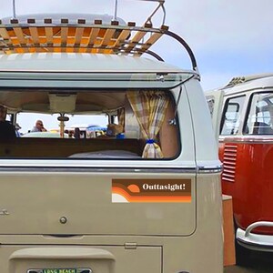 May include: A vintage white van with a wooden roof rack and a retro-style sticker on the back that says "Outtasight!" The sticker features a sunset and wavy lines in orange, brown and yellow.