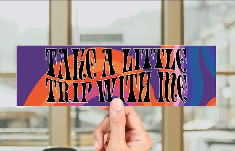 May include: A colorful sticker with the text "Take a little trip with me" in a retro font. The sticker has a purple, orange, pink, and blue background with a wavy pattern.