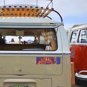 May include: A white vintage van with a wooden roof rack and a colorful sticker on the back that says "Take a little trip with me".