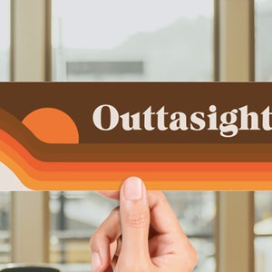May include: A brown and orange retro-style bumper sticker with the text "Outtasight!" in white. The sticker features a stylised sunset design.