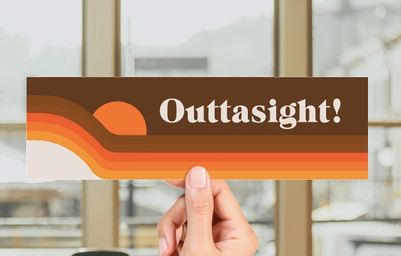 May include: A brown and orange retro-style bumper sticker with the text "Outtasight!" in white. The sticker features a stylised sunset design.