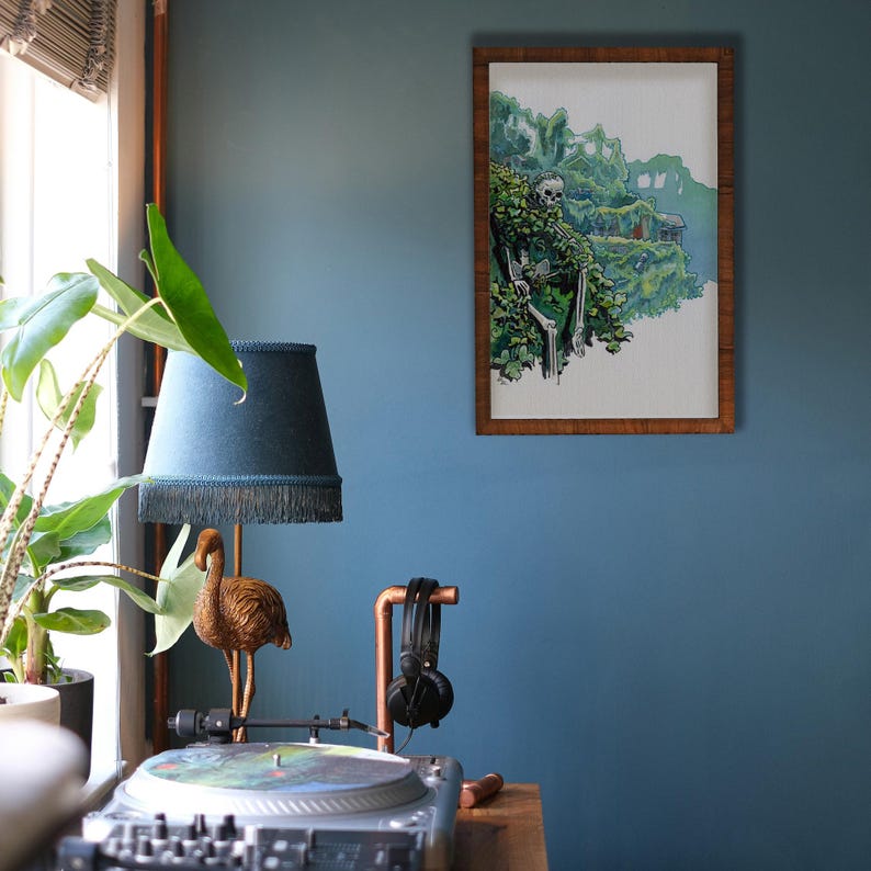 May include: A framed illustration of a skeleton sitting in a lush green jungle with a waterfall in the background. The frame is brown wood and the illustration is in watercolor style.