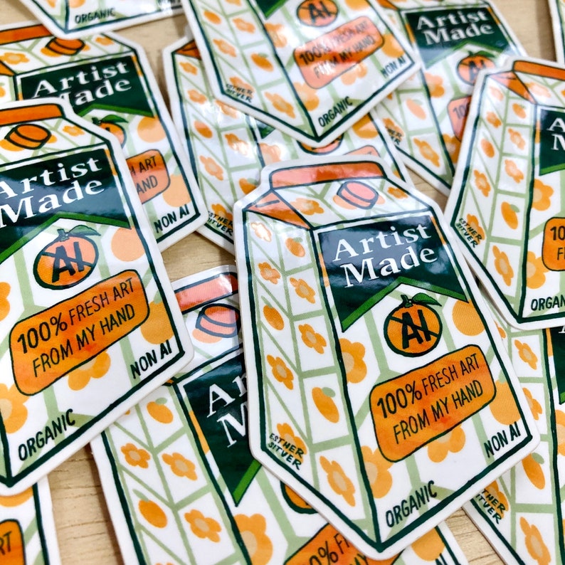May include: A close-up of several stickers with a cartoon illustration of a juice carton. The carton is orange and green with a white background. The text on the carton reads "Artist Made" and "100% Fresh Art From My Hand". The stickers are all organic and non-AI.
