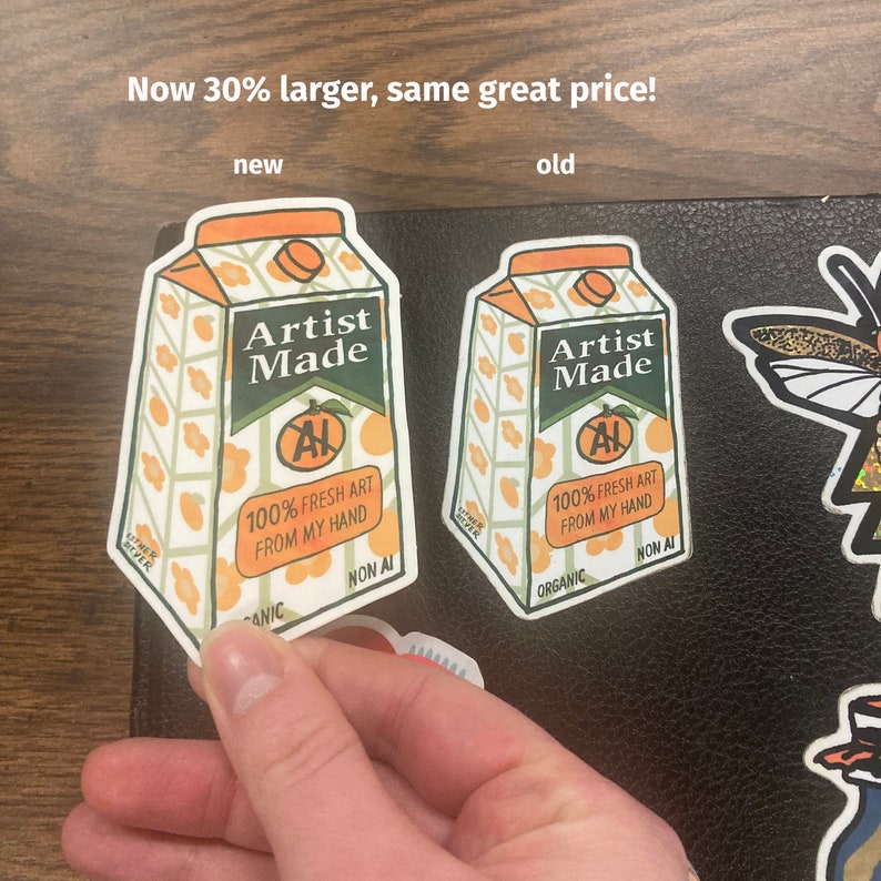 May include: Two orange juice carton stickers, one larger than the other. Both stickers feature the text "Artist Made" and "100% Fresh Art From My Hand". The larger sticker is labeled "new" and the smaller sticker is labeled "old".