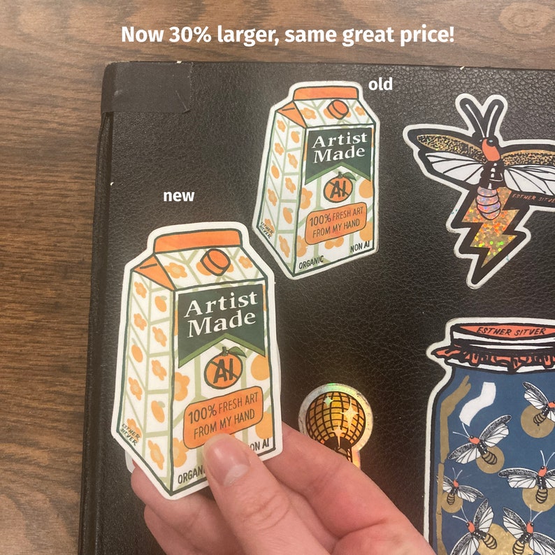 May include: Two versions of a sticker for a product called "Artist Made". The sticker is shaped like a juice box with an orange design. The text on the sticker says "100% Fresh Art From My Hand". The smaller sticker is labeled "new" and the larger sticker is labeled "old".