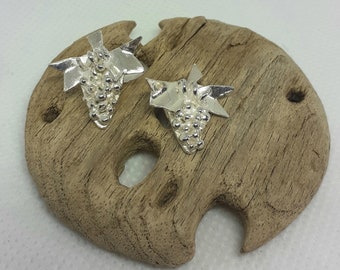 May include: A pair of silver earrings shaped like bunches of grapes. The earrings are on a wooden surface.