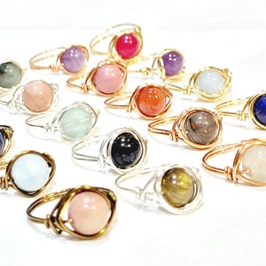 May include: A collection of wire-wrapped rings featuring various gemstones, including amethyst, rose quartz, carnelian, aquamarine, lapis lazuli, and tiger's eye.