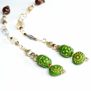 May include: A pair of long, gold chain earrings with green and gold beads. The beads have a textured, patterned surface.