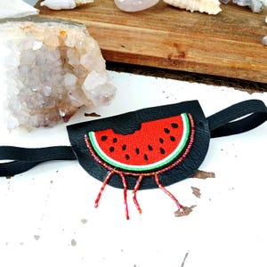 Può includere: Maschera per gli occhi nera con un design a forma di anguria. La maschera presenta una fetta di anguria rossa con semi neri, una buccia verde e un bordo di perline. La maschera ha un elastico per una vestibilità sicura.