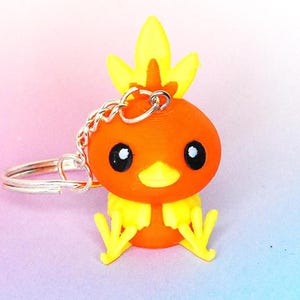 Op de afbeelding: Oranje en gele 3D-geprinte sleutelhanger van een cartoonvogel met een vlam op zijn kop.