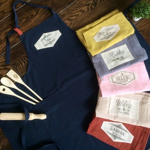 Custom linen cotton aprons premium size in navy blue, mustard yellow, grey, pink and tile red colors. For the hand printed custom tag you can choose from many graphics and your text, names and dates. Unique quality couple gift.