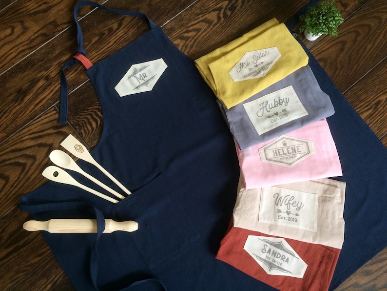 Custom linen cotton aprons premium size in navy blue, mustard yellow, grey, pink and tile red colors. For the hand printed custom tag you can choose from many graphics and your text, names and dates. Unique quality couple gift.