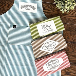 Classic striped quality cotton aprons in green, blue, beige, red and white stripes. Customized with hand printed graphic patches and the text, date and names you want. The unique custom gift for anniversaries, weddings, birthdays.