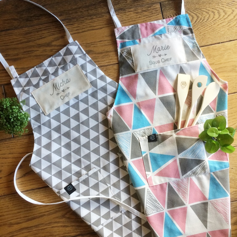 Custom hand printed Chef and sous chef aprons from graphic pattern aprons ingrey and white triangles and pink, grey blue and white triangle pattern. The ideal custom couple gift for him and her, for anniversaries, birthdays and more.