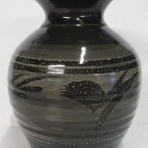 May include: A dark grey ceramic vase with a wide base and a narrow neck. The vase features horizontal bands and a stylized black design with white speckles. The vase is approximately 20 cm tall.