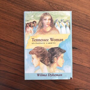 May include: A book cover with a blue sky background and a painting of a woman with a headband. The title of the book is "Tennessee Woman: An Infinite Variety" by Wilma Dykeman.