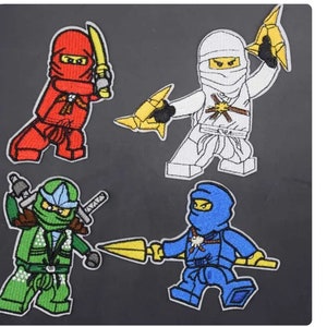 Könnte beinhalten: Vier aufgestickte Aufnäher mit Ninja-Charakteren in Rot, Weiß, Grün und Blau. Jeder Ninja befindet sich in einer dynamischen Pose und hält Waffen wie Schwerter und Wurfsterne. Die Aufnäher befinden sich auf einem dunkelgrauen Hintergrund.