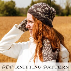 May include: A woman wearing a white coat and a brown and white patterned knit hat and gloves. The hat has a unique design with a floral pattern. The woman is standing in a field of golden wheat.
