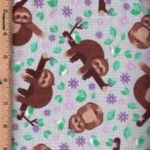 May include: A gray fabric with a repeating pattern of brown sloths hanging from branches with green leaves and purple flowers. Small blue birds are also included in the pattern.