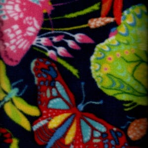 Puede incluir: Primer plano de una tela con fondo azul oscuro, con un vibrante estampado de mariposas y libélulas de colores. Las mariposas son en tonos rosa, rojo, amarillo y azul, mientras que las libélulas son verdes y amarillas. La tela tiene un aspecto suave y texturizado.