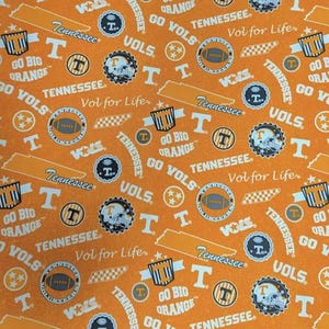 Pode incluir: Um tecido laranja com um padrão repetitivo de logotipos esportivos dos Tennessee Volunteers, incluindo bolas de futebol americano, o contorno do estado, a letra T e textos como Go Vols, Go Big Orange, Tennessee e Vol for Life em branco e azul marinho.