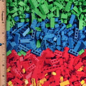 Könnte beinhalten: Ein farbenfrohes Bild von Spielzeugbausteinen in Grün, Blau, Rot und Gelb. Die Steine sind über das Bild verstreut, mit einem Lineal auf der linken Seite. Das Bild ist eine Nahaufnahme der Steine.