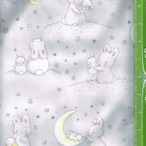 May include: A white fabric with a repeating pattern of bunnies holding smaller bunnies. The background is light blue with yellow stars and a crescent moon.