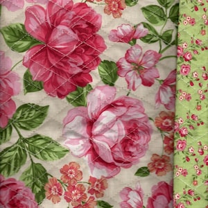 Pode incluir: Um tecido acolchoado com um padrão floral que apresenta rosas rosa e brancas, folhas verdes e pequenas flores rosa e laranja sobre um fundo creme.