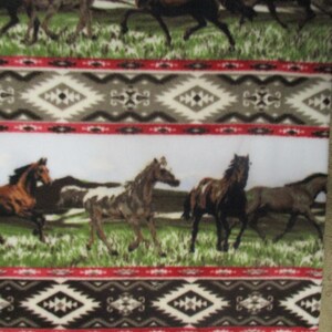 May include: White fabric with a repeating pattern of running horses in a grassy field. The design includes a southwestern-style border with geometric shapes in black, gray, and red. The horses are various shades of brown and white.