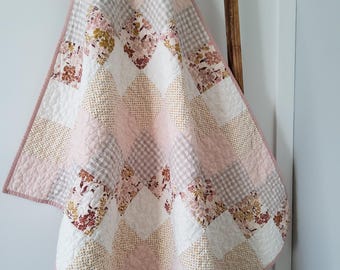 May include: A pink, white, and brown patchwork quilt with a floral pattern. The quilt is folded and hanging on a wooden ladder.