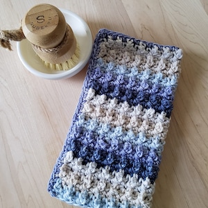 May include: A blue, purple, and beige crocheted dishcloth with a textured pattern.