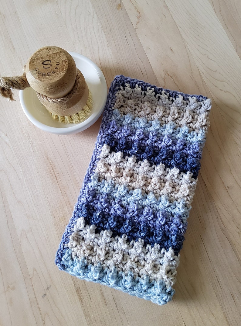 May include: A blue, purple, and beige crocheted dishcloth with a textured pattern.
