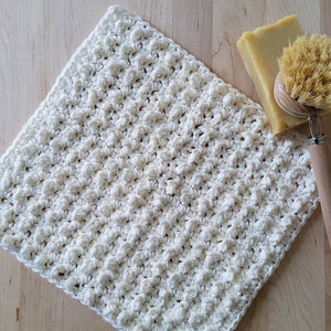 May include: A white crocheted dishcloth with a textured surface. The dishcloth is made of cotton yarn and is perfect for cleaning dishes or wiping down surfaces.