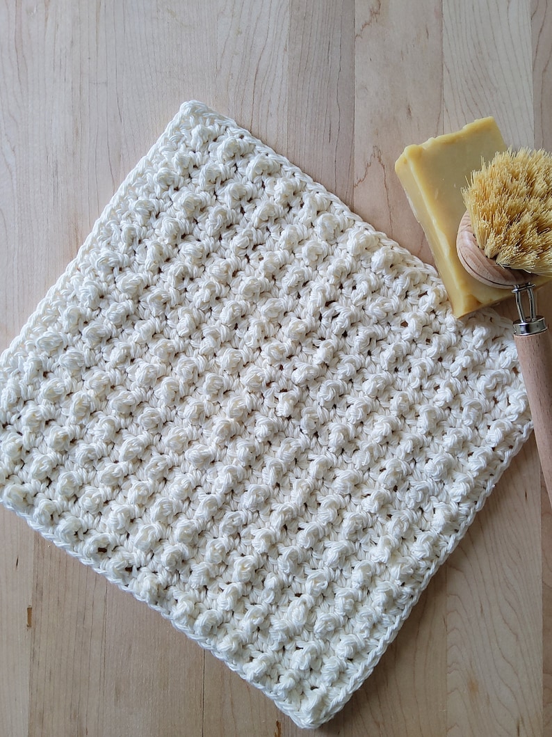 May include: A white crocheted dishcloth with a textured surface. The dishcloth is made of cotton yarn and is perfect for cleaning dishes or wiping down surfaces.
