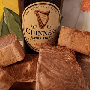 May include: Four bars of brown and tan soap with a bottle of Guinness Extra Stout beer in the background. The bottle label reads "Traditionally Brewed, Est. 1759, Guinness Extra Stout".