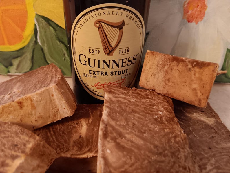 May include: Four bars of brown and tan soap with a bottle of Guinness Extra Stout beer in the background. The bottle label reads "Traditionally Brewed, Est. 1759, Guinness Extra Stout".