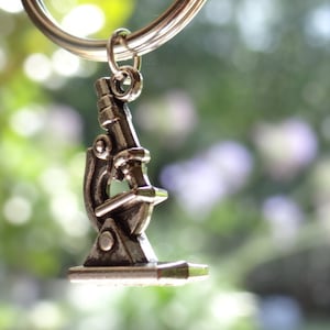 May include: A silver microscope keychain with a detailed design. The keychain is hanging from a silver ring.