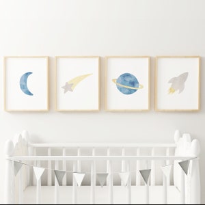 May include: Four framed watercolor prints with a space theme. The prints feature a crescent moon, a shooting star, a planet with rings, and a rocket ship. The prints are in shades of blue, yellow, and gray.