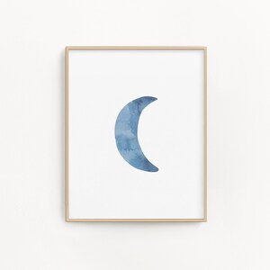 May include: A framed print of a blue watercolor crescent moon on a white background.
