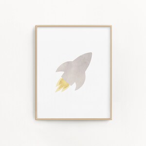 May include: A framed print of a watercolor illustration of a gray rocket with a yellow flame. The rocket is flying to the right.