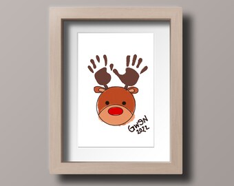 May include: A framed handprint art piece of a reindeer with brown antlers and a red nose. The reindeer's face is brown and the background is white. The text "GWYSN 2022" is written in black ink in the bottom right corner.