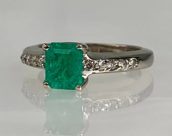 May include: A silver ring with a large emerald green gemstone and a band of small diamonds.